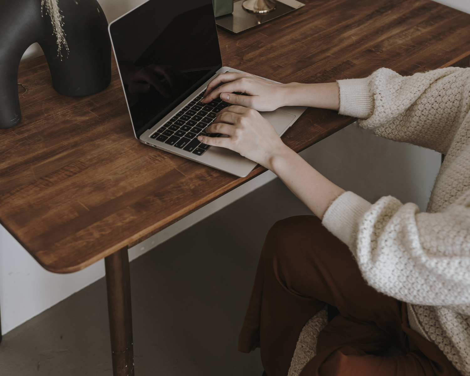 Email Marketing Laws - what you need to know. Photo of woman typing on computer wearing a white sweater. Brown desk with decor.